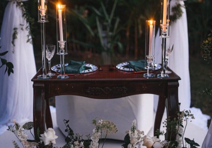 A table with two candles on it and flowers around.